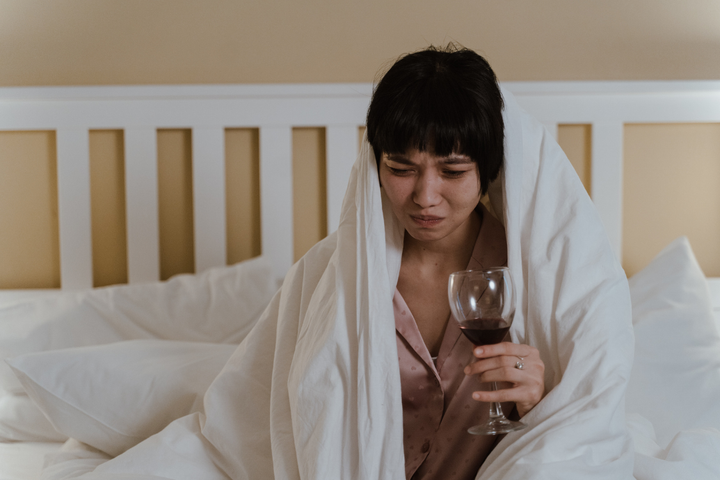 Woman wrapped in blanket holding a glass of wine, feeling unwell — illustrating NAC for hangover recovery.