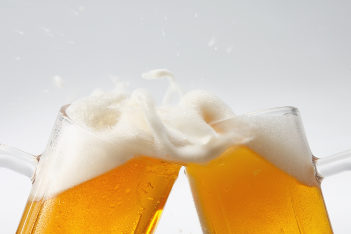 Close-up of two beer mugs clinking, with foam splashing out, illustrating the fluid content and the topic: is non-alcoholic beer hydrating?