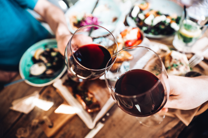 Two people clinking glasses of red wine over a meal, symbolizing eating before drinking alcohol.