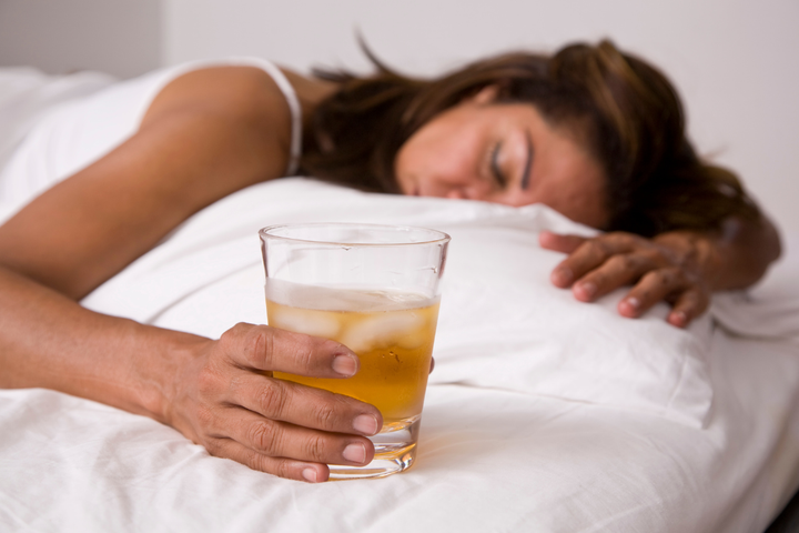 A woman rests in bed with a glass of ice-filled drink nearby, focusing on rest and recovery from hangxiety.